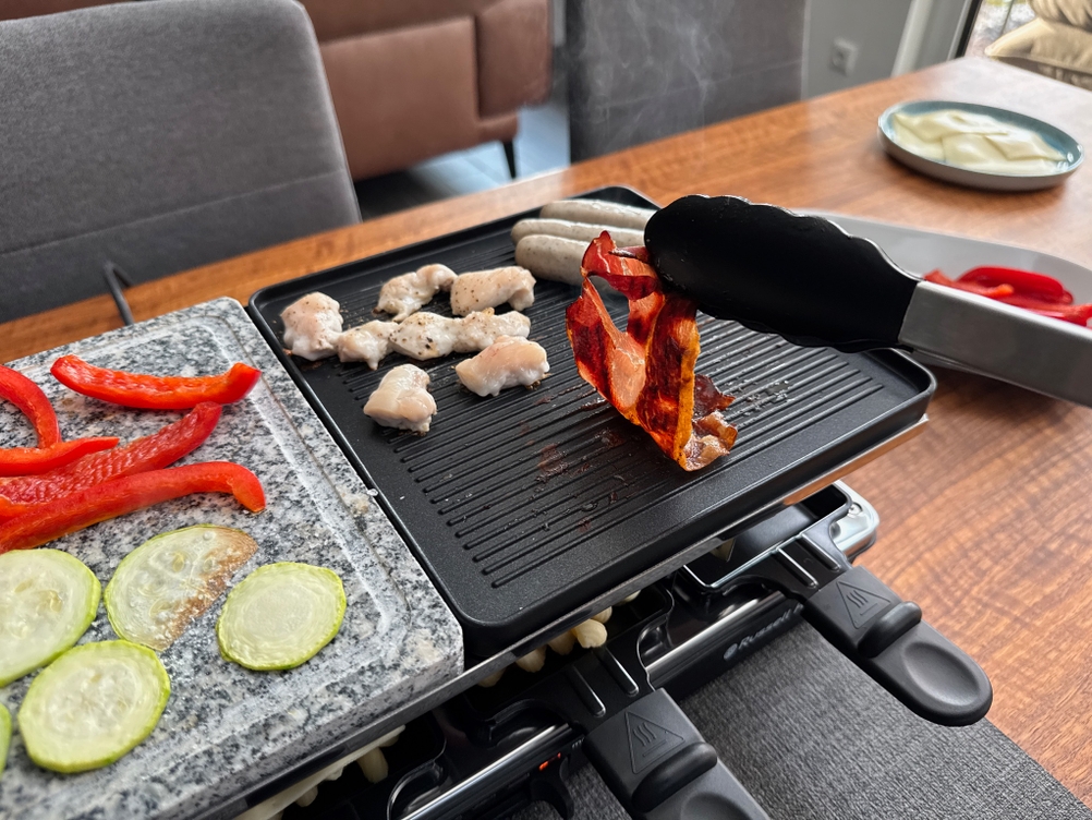 Mit einer Grillzange wird Speck von der Grillplatte des Russell Hobbs 26280-56 entfernt.