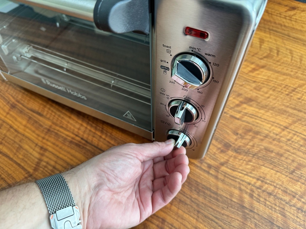 Eine Hand stellt etwas an einem Drehregler des Russell-Hobbs-Minibackofen Express Airfry 5-in-1 26095-56 ein