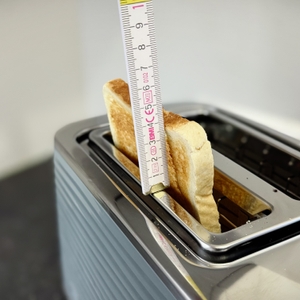 Aus dem getesteten Toaster steht eine fertige Toastscheibe heraus und eine Person misst mit einem Meterstab wie weit diese heraussteht.