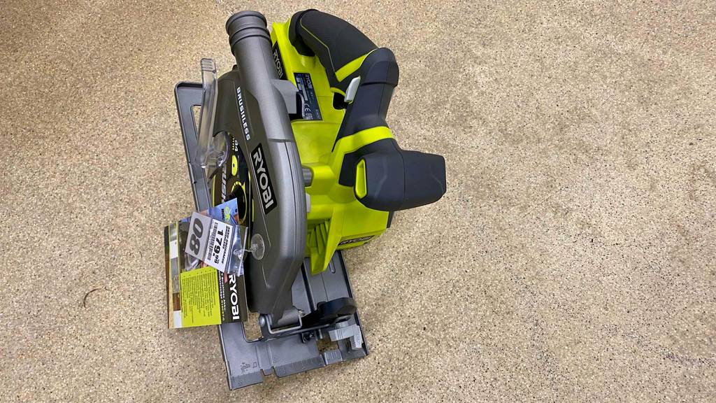 Ansicht von oben auf eine auf beigefarbenen Boden stehende gelb-graue Ryobi Kreissäge im Test, mit Fokus auf den Softgripp-Griff.