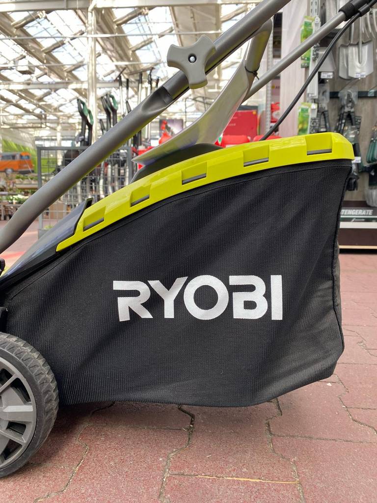 Seitenansicht auf den schwarzen Fangkorb eines getesteten Rasenmähers mit Mulchfunktion der Marke Ryobi in einem Gartencenter.
