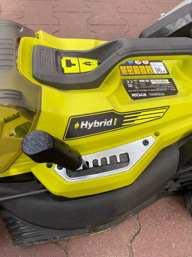 Seitenansicht auf die gelb verkleidete Motoreinheit inklusive Gangschaltung eines getesteten Rasenmähers mit Mulchfunktion der Marke Ryobi, der in einem Gartencenter ausgestellt ist.