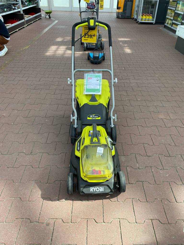 Ansicht von vorn auf den gelb-schwarzen Rasenmäher mit Mulchfunktion im Test, der Marke Ryobi, der in einem Gartencenter ausgestellt ist.