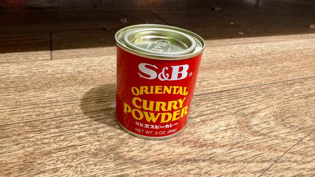 Eine Blechdose mit getestetem Currypulver steht auf einer Holzfläche.