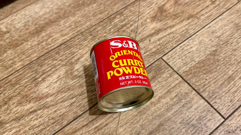 Eine Dose mit Currypulver im Test liegt auf einer Holzfläche.