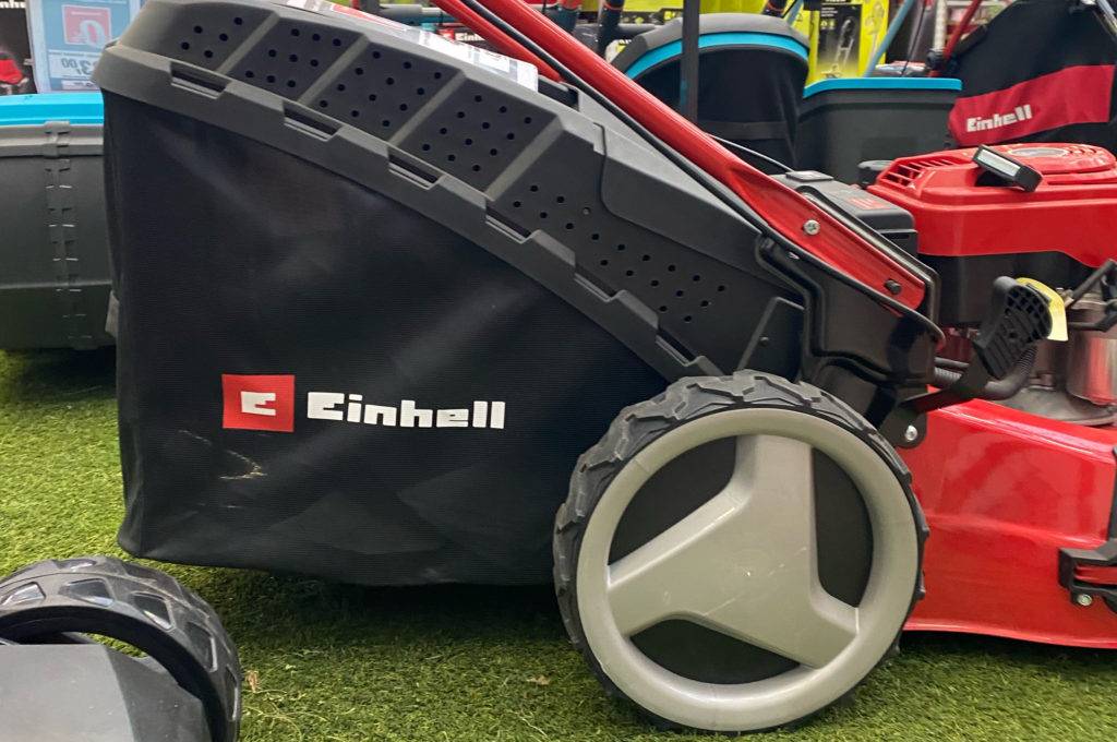 Reifen und Auffangbehälter eines getesteten Benzin Rasenmähers mit 51 cm Schnittbreite, der auf Kunstrasen steht.