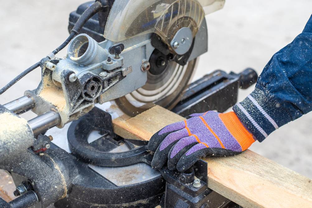 Sägeblatt (160x20) im Test: Eine Person mit einem Sicherheitshandschuh schneidet mit einer Kappsäge ein Brett ab. 