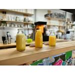 Orangensaft aus 3 verschiedenen Saftpressen stehen in kleinen Flaschen nebeneinander.