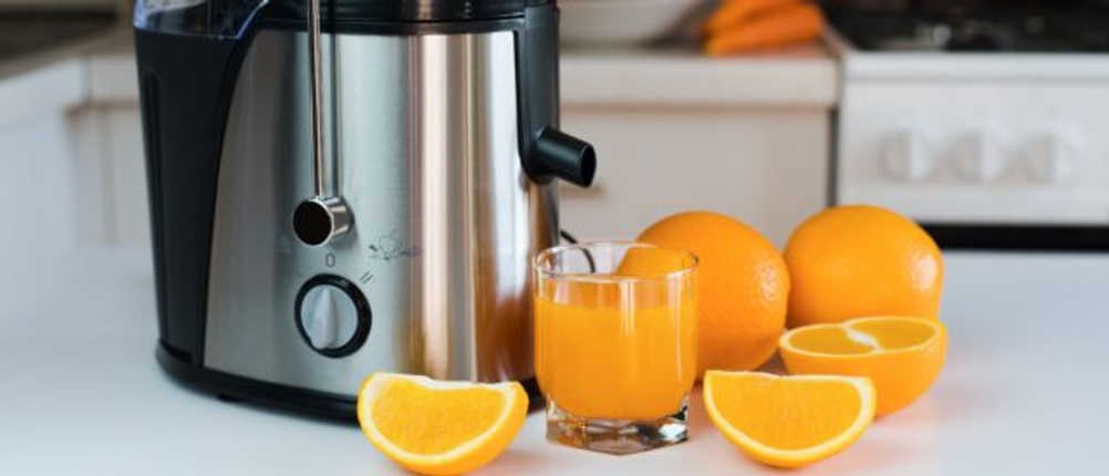 Eine moderne Saftpresse steht neben einem Glas Orangensaft und mehreren Orangen