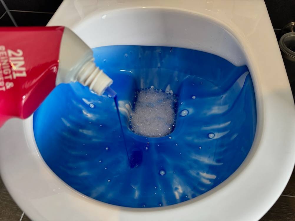 Sagrotan-WC-Reiniger Blütenfrische wird mit intensiver blauer Farbe in die Toilette gegeben.