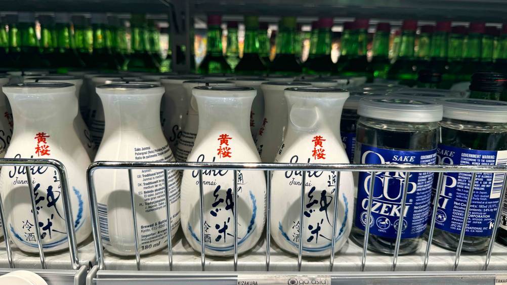 Mehrere Flaschen des getesteten Sake in einem Regal neben anderen Flaschen.