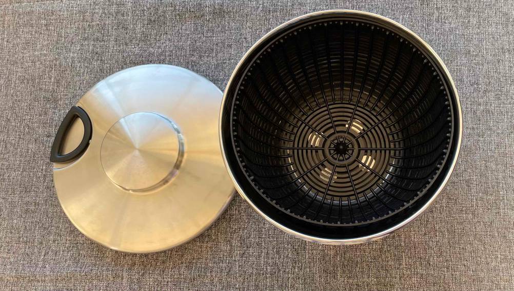 Getestet: Eine Edelstahl-Salatschleuder mit Einsatz neben ihrem Deckel auf einer grauen Fläche.