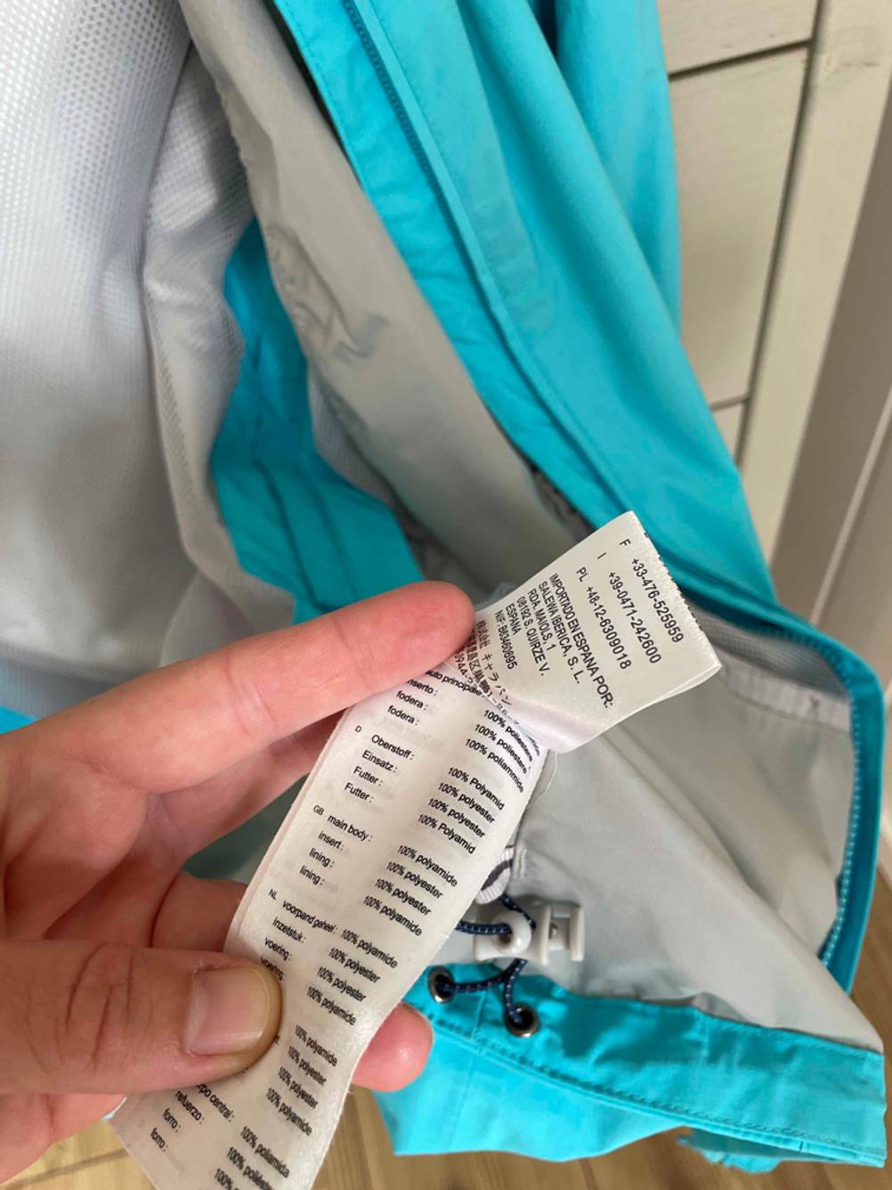 Hand zeigt das Etikett einer getesteten Regenjacke für Damen.