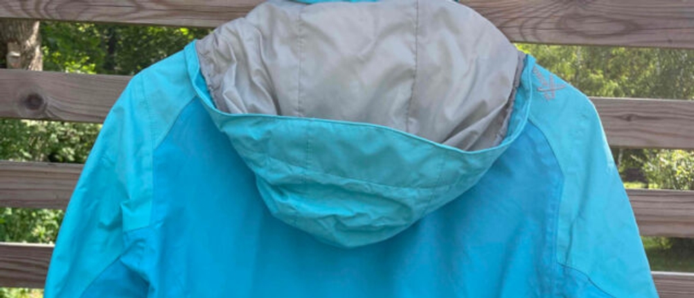 Regenjacke für Damen im Test: Eine blaue Jacke hängt mit der Rückseite nach vorn an einem Holzzaun.