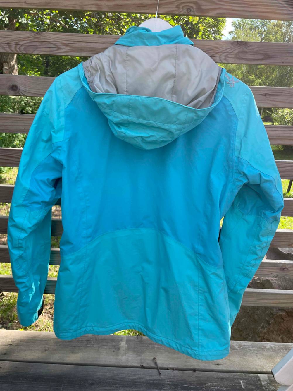 Regenjacke für Damen im Test: Eine blaue Jacke hängt mit der Rückseite nach vorn an einem Holzzaun.