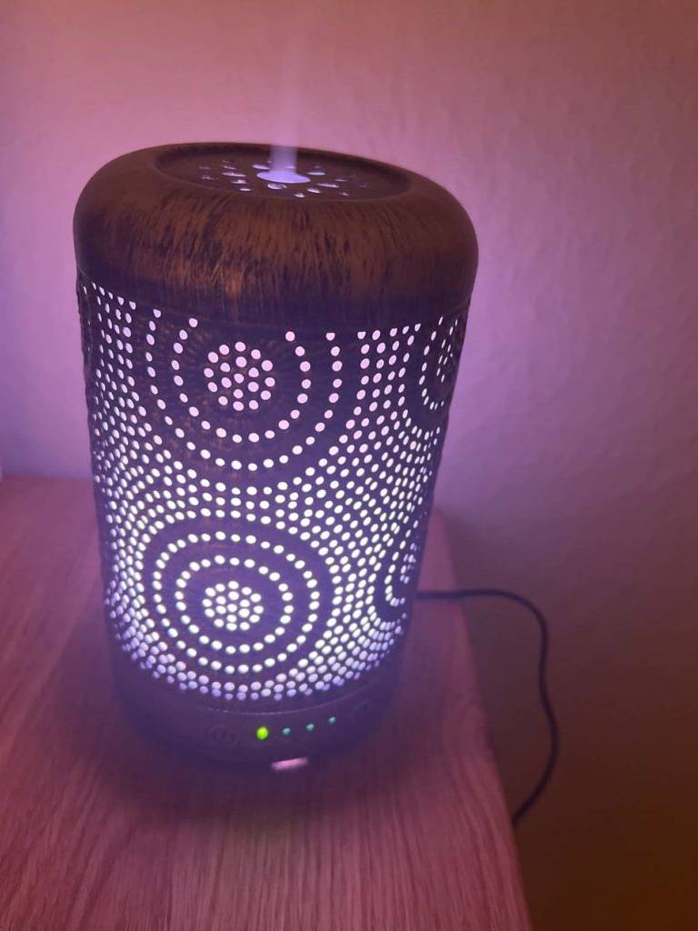 Nahaufnahme von einem eingeschalteten, metallischen, mit Lochdesign und Beleuchtung versehenen Diffuser im Test in dunkelrotem Ambiente.