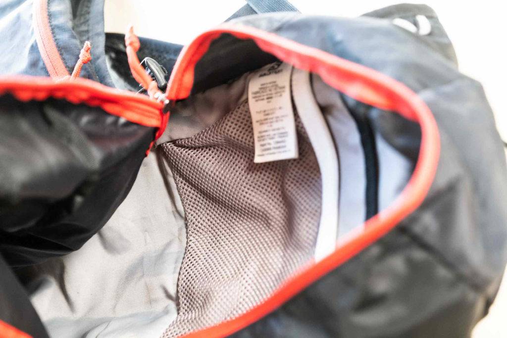 Nahaufnahme des Innenraums eines mit rotem Reißverschluss geöffneten Fachs inklusive Produktetikett von einem schwarzen getesteten Laufrucksack.