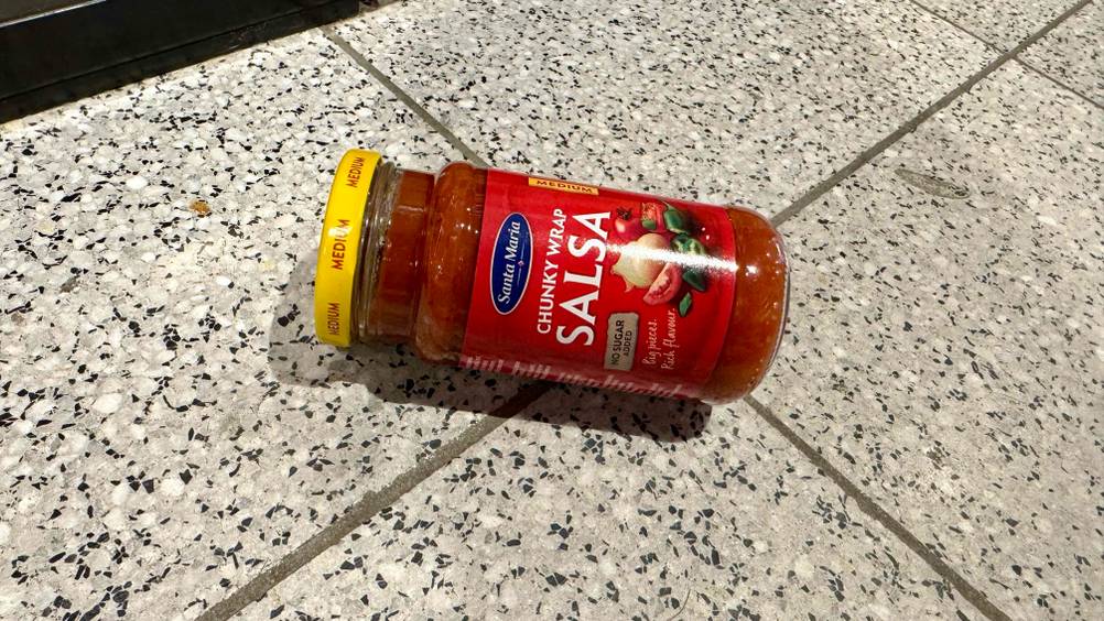 Ein Glas der getesteten Salsa auf einem Fließenboden.