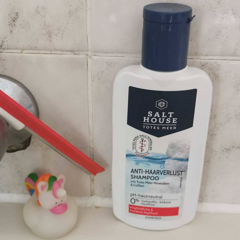 Eine Packung Salt House Anti Haarverlust Shampoo steht auf dem Badewannenrand.