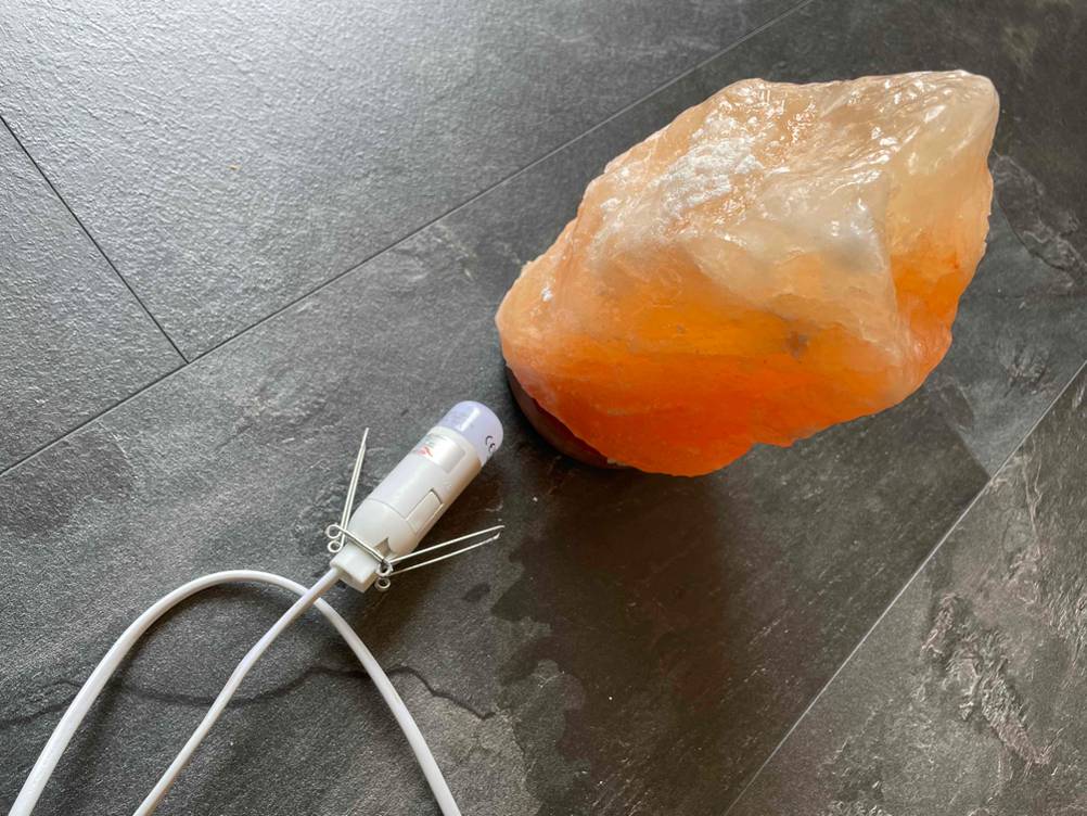 Eine getestete Salzlampe, daneben die Glühlampe in der Fassung mit Kabel auf einer dunklen Fläche.