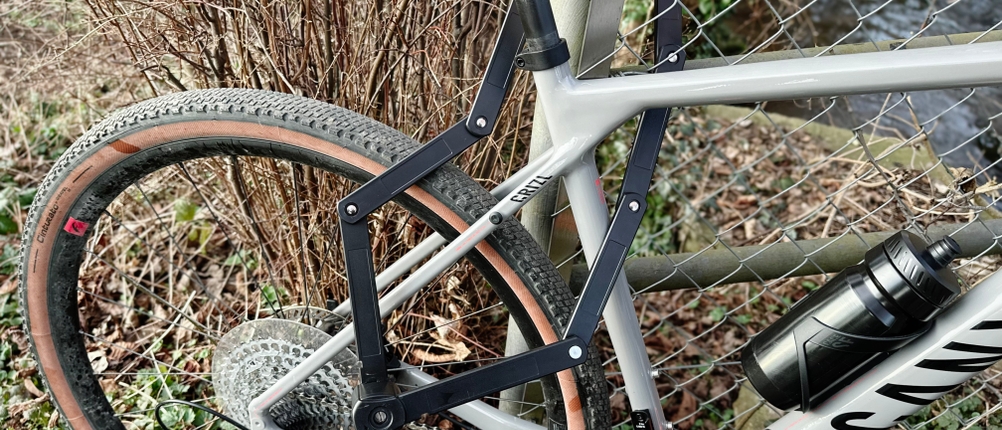 Das Samok-Klappradschloss ist um Fahrradrahmen und Zaunpfosten gelegt. Das Fahrrad steht am Straßenrand.