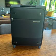 Der Samsonite Base Boost Upright steht auf seinen Rollen auf einem Holztisch.