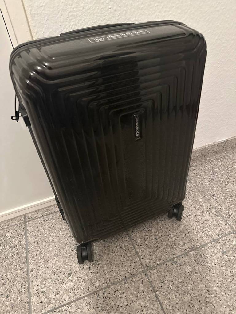 Ansicht von schräg oben auf einen Samsonite Handgepäck-Koffer im Test auf grauem Fliesenboden vor weißer Wand.
