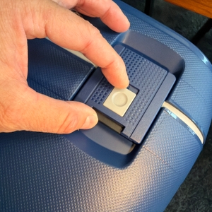 Eine Hand entriegelt den Samsonite S'Cure Spinner 75/28.