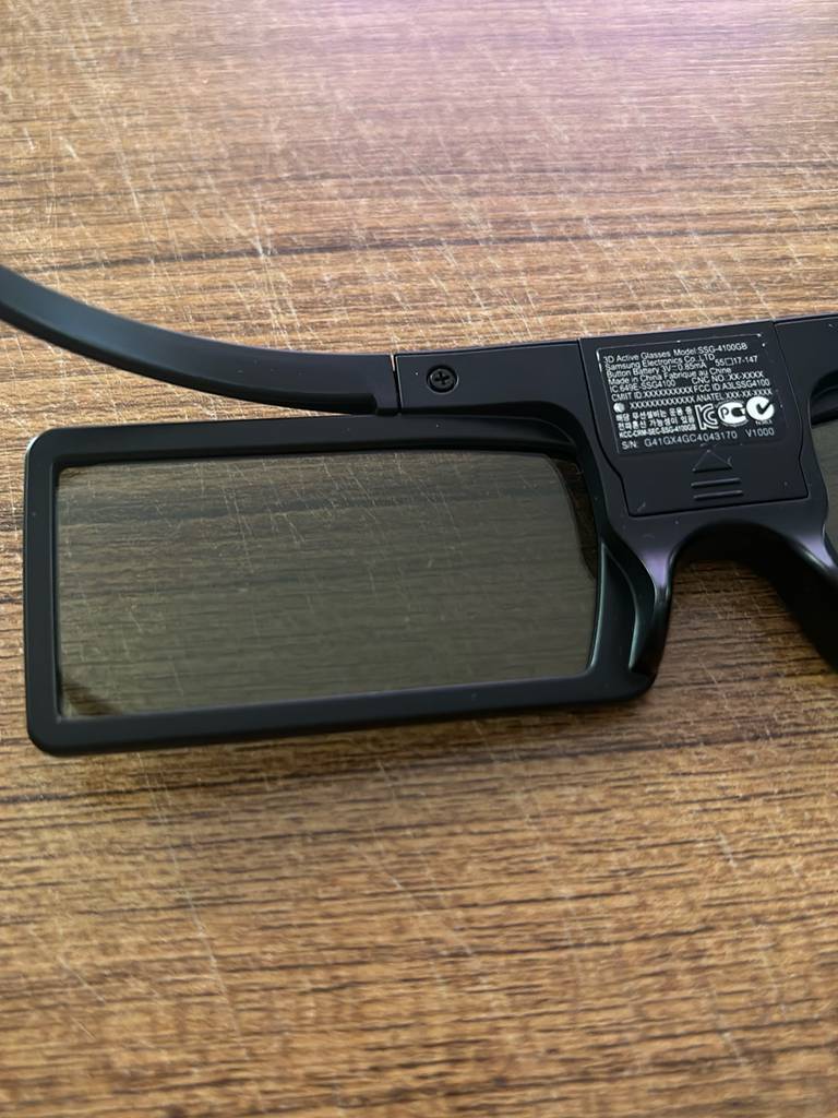 Detailansicht des Glases einer schwarzen 3D-Brille im Test mit rechteckigem Rahmen vor einem Holzhintergrund.