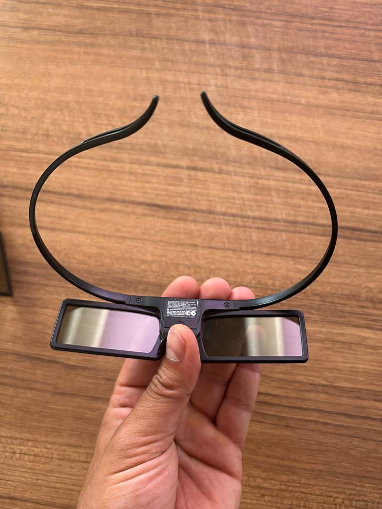 Hand hält eine schwarze 3D-Brille im Test, mit Blick auf das innen angebrachte Produktschild vor einem Holzhintergrund.