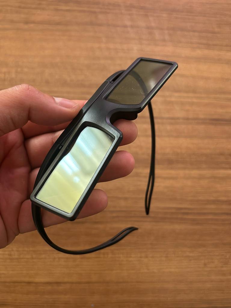 Hand hält eine 3D-Brille im Test vor einem Holzhintergrund.