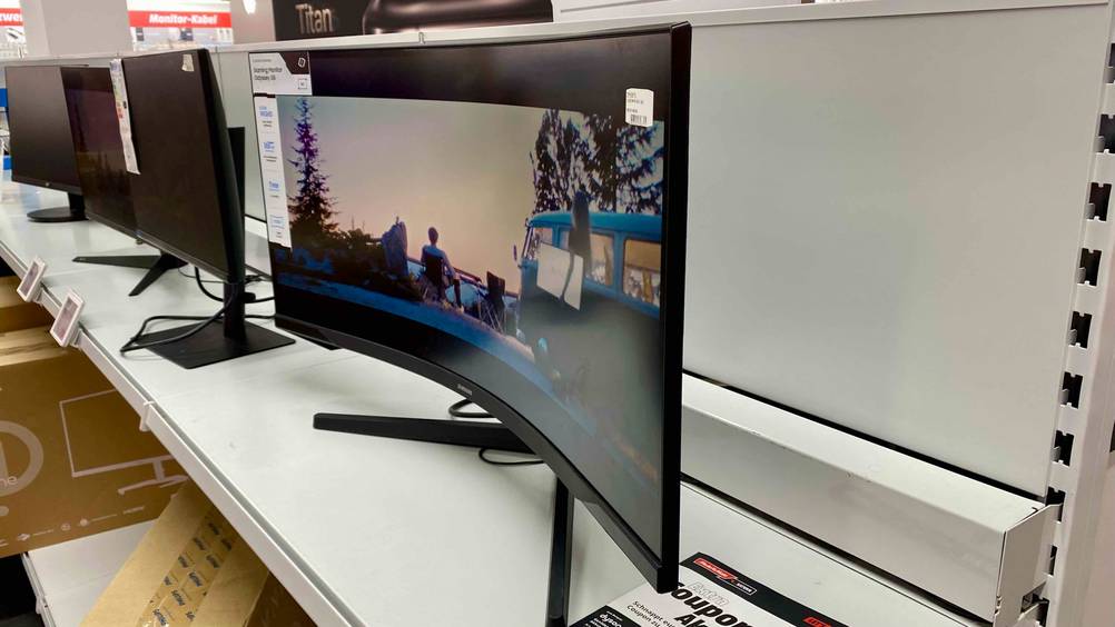 Im Test: Ein Curved-Gaming-Monitor von der Seite in einer Ausstellung im Hintergrund weitere Geräte.