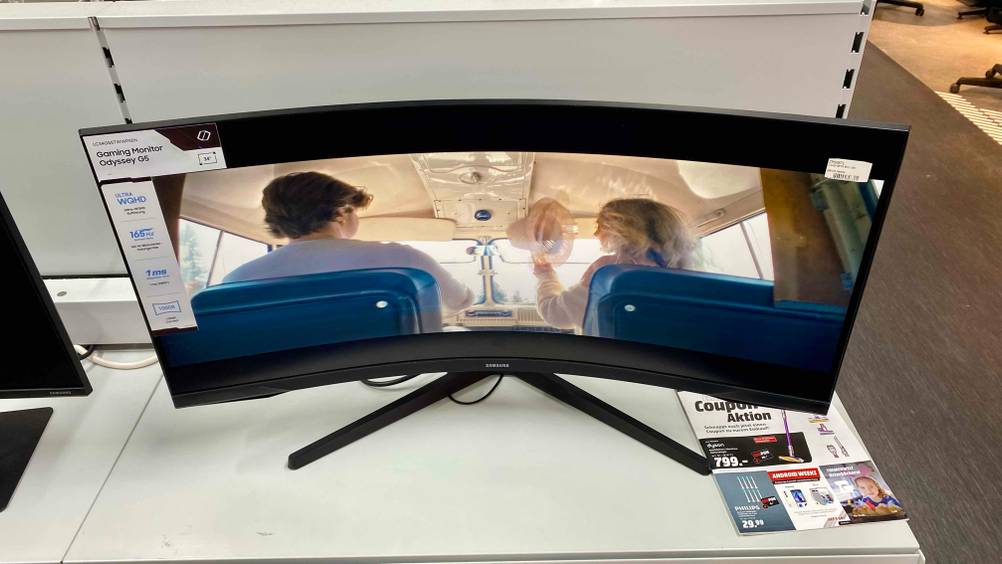 Ein getesteter Curved-Gaming-Monitor auf einem hellen Regal in einer Ausstellung von schräg oben.