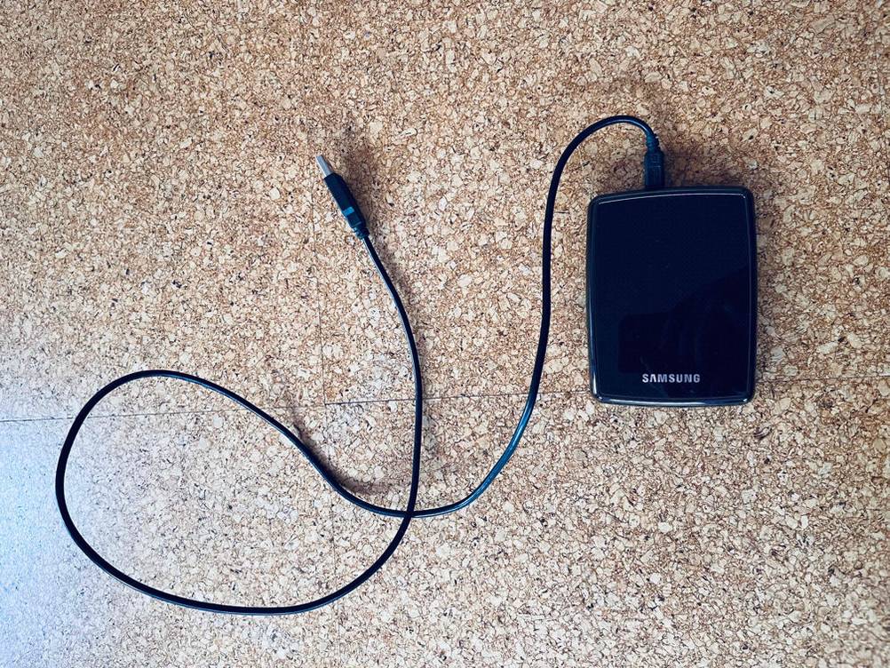 HDD-Festplatten mit 3,5 Zoll im Test: ein Samsung Modell in Schwarz liegt mit einem angeschlossenen USB-Kabel auf braun gesprenkelten Fliesen.
