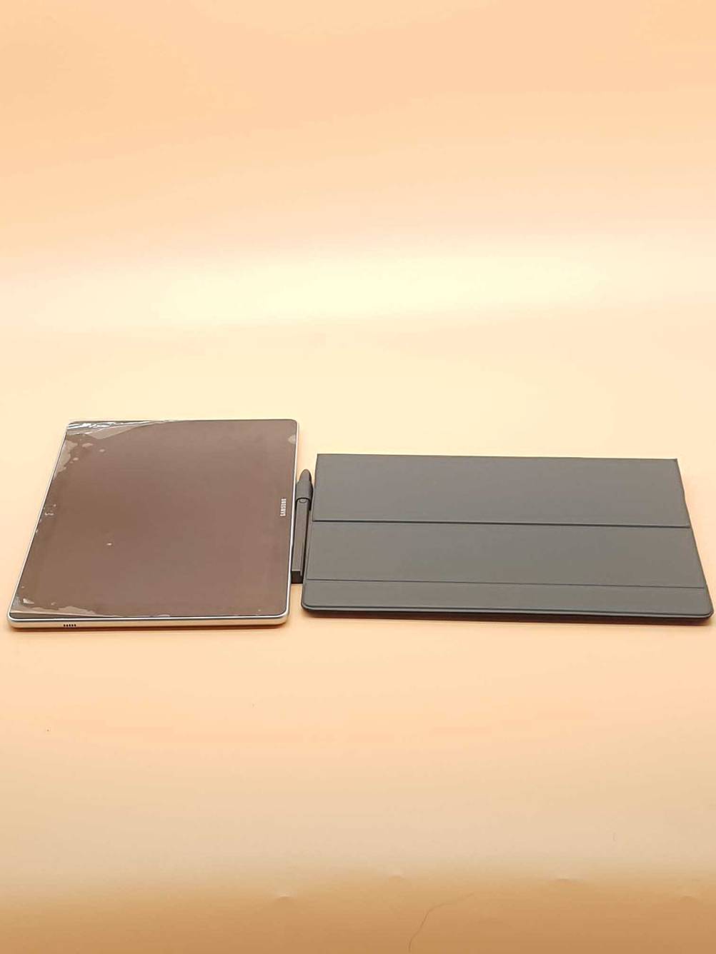 Samsung Galaxy Book-Test: Ein Gerät, ein Stift und die Hülle nebeneinander auf einer orangen Fläche.