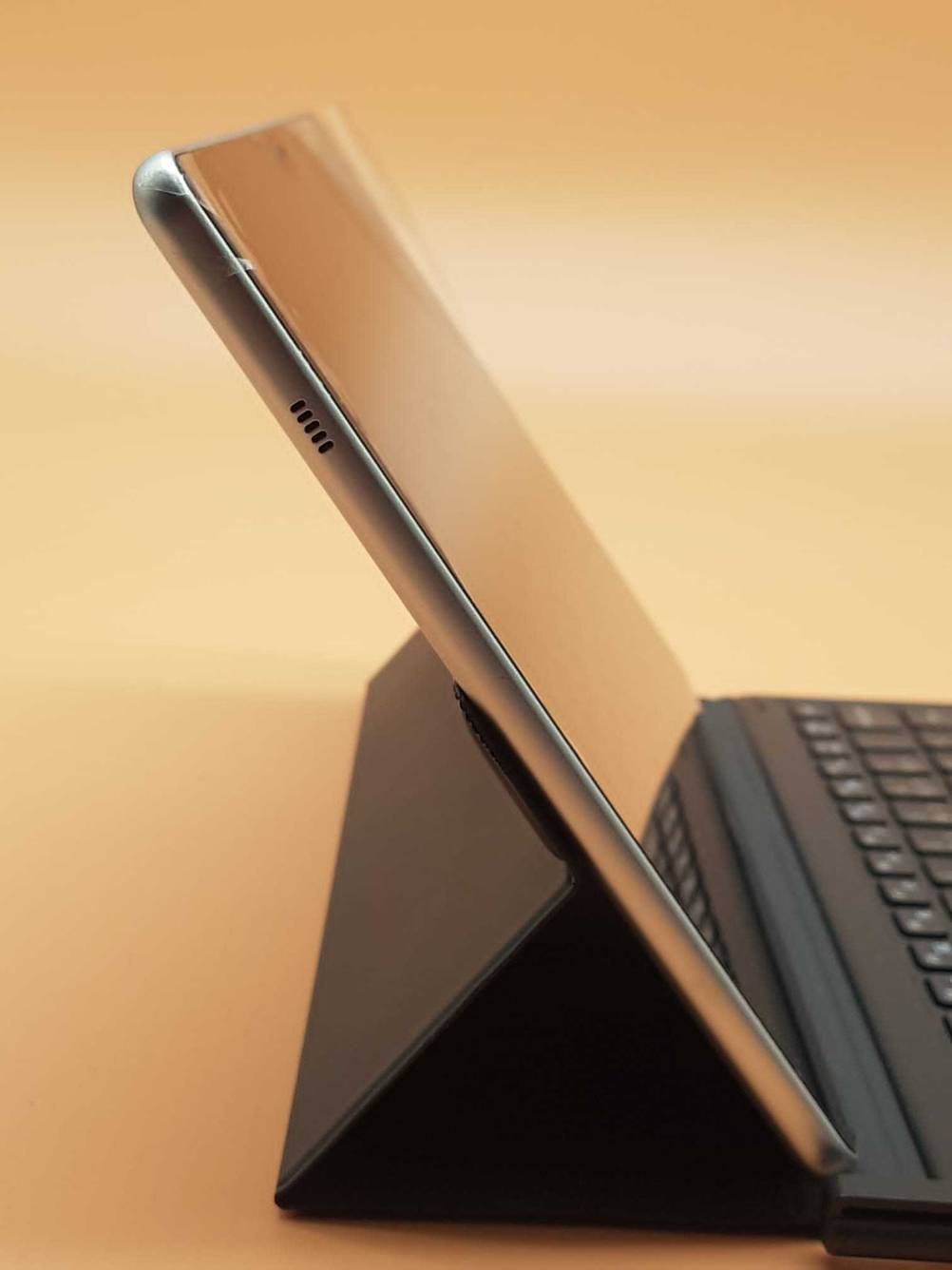 Ein Samsung Galaxy Book im Test von der Seite mit einer Tastatur und einem Ständer vor einer orangen Fläche.