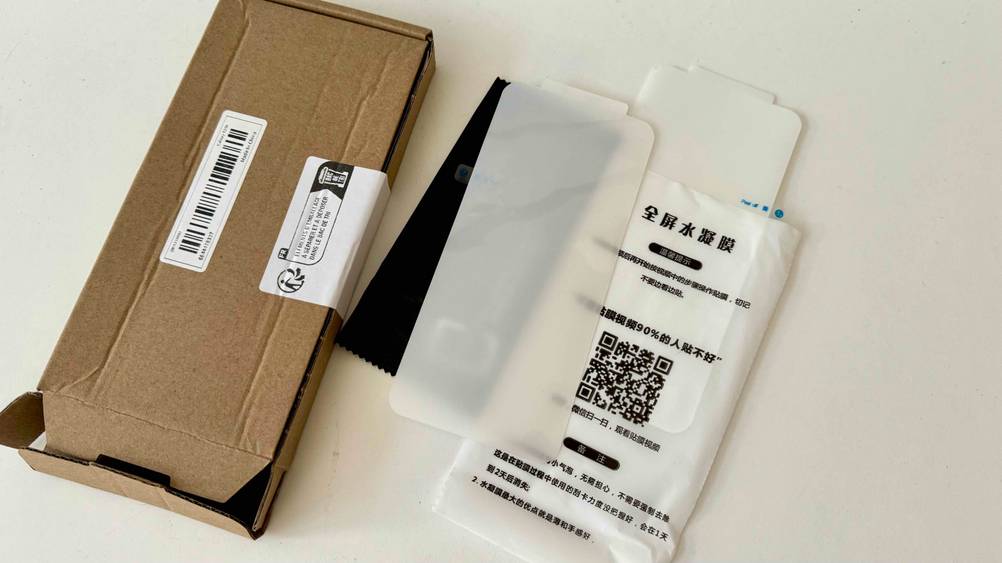 Neben einem Karton liegt das getestete Samsung-Galaxy-S20-Plus-Panzerglas mit Hülle und Tuch.