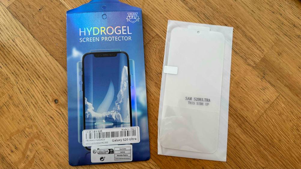 Getestet: Eine Samsung-Galaxy-S20-Ultra-Panzerglas liegt auf einer Holzfläche neben der Origialverpackung.