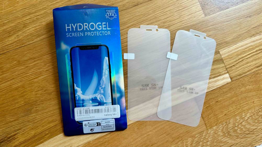 Auf einem Holzboden liegen die Originalverpackung und zwei Samsung-Galaxy S8-Plus-Panzergläser im Test.
