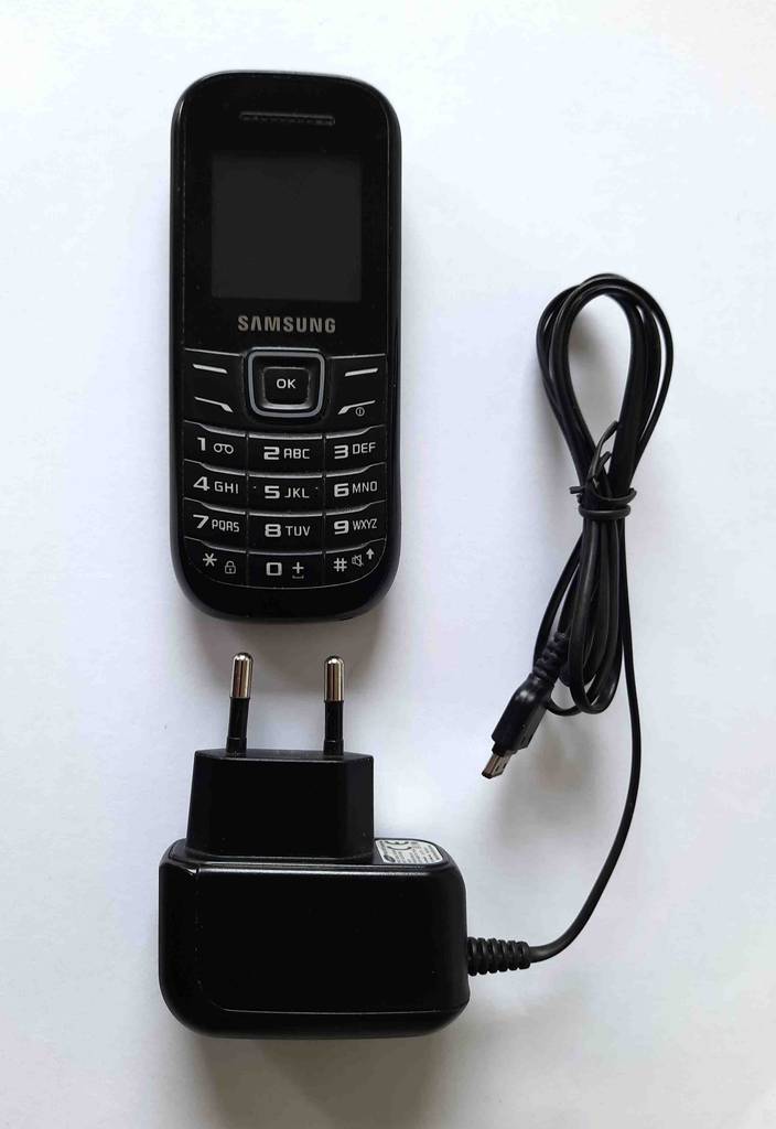 Tastenhandy-Test: Ansicht von oben auf ein schwarzes Modell von Samsung inklusive Kabel und Adapter auf einem weißen Untergrund.