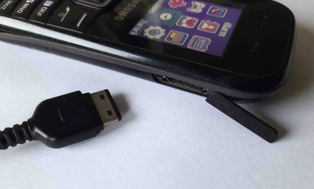 Tastenhandy im Test: Nahaufnahme des geöffneten Ladeanschlusses, neben dem ein USB-Kabelstecker auf weißer Fläche liegt.