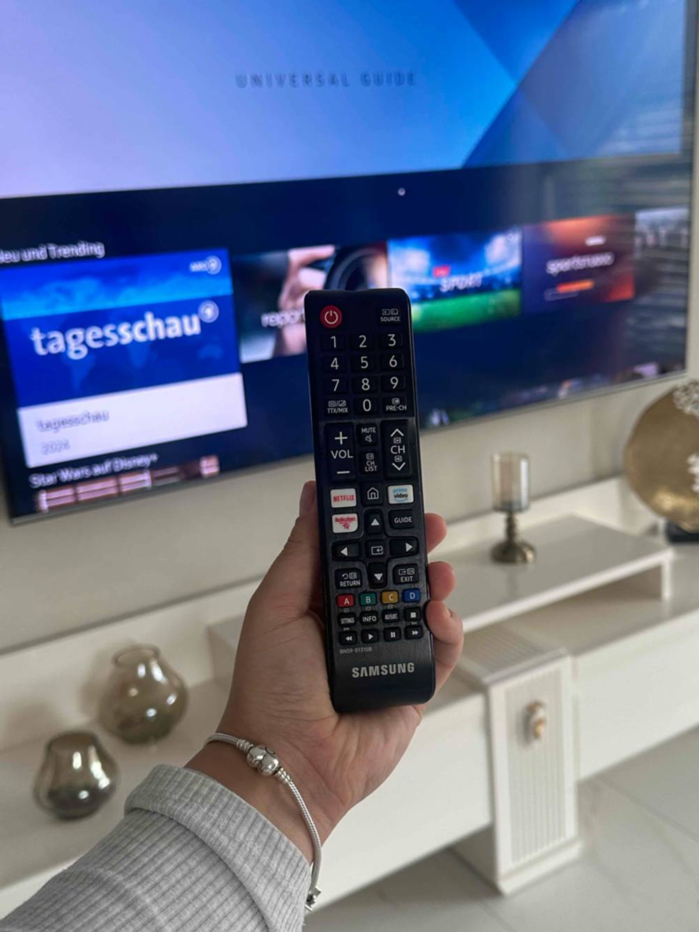 Eine Hand bedient die Fernbedienung eines eingeschalteten 80-Zoll-Fernsehers im Test.