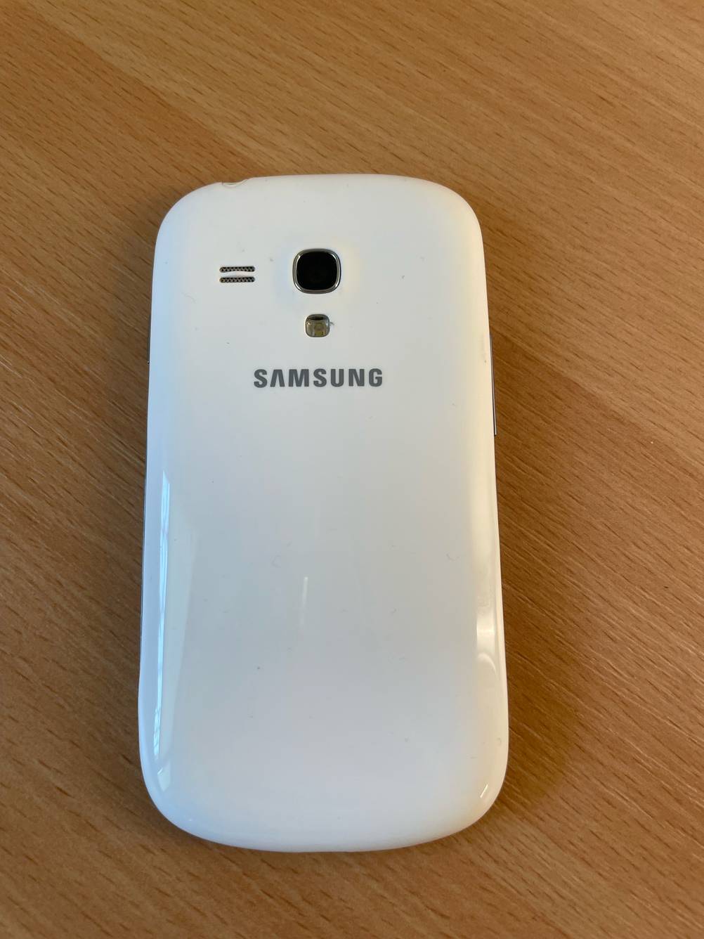 Ein getestetes Samsung-Handy bis 300 Euro mit der Rückseite nach oben auf einer Holzfläche.