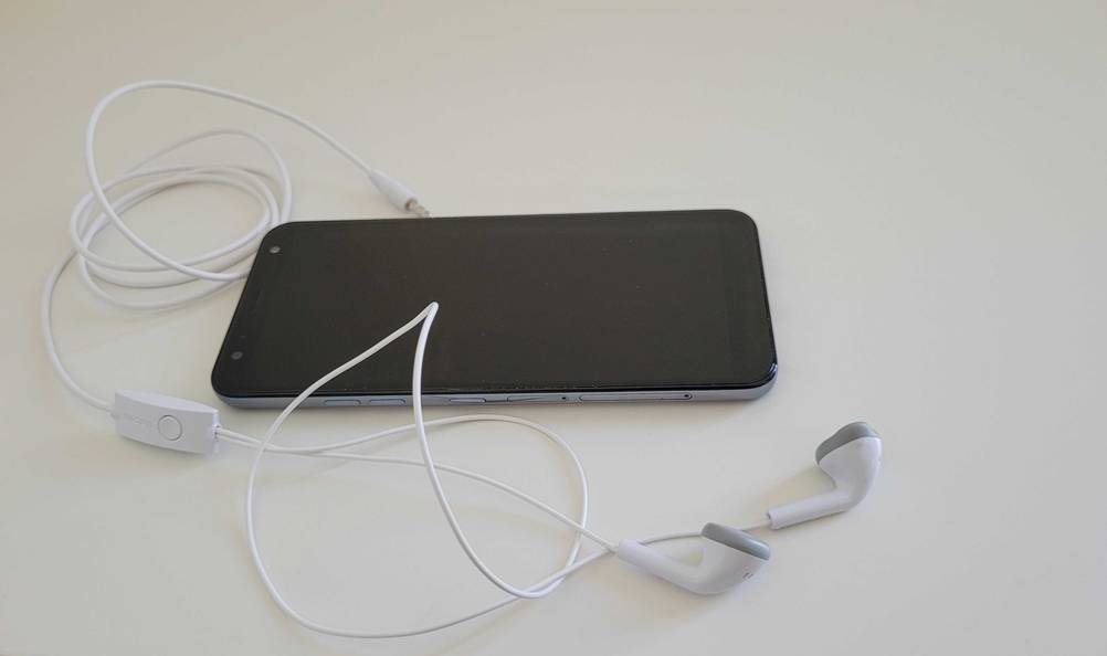 Neben einem Handy liegen die getesteten Samsung-In-Ear-Kopfhörer auf einer hellen Fläche.