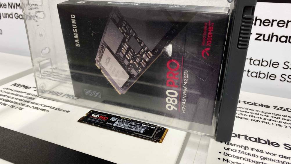 Eine getestete M.2-SSD (500 GB) in einer Infofläche eingebettet, dahinter die Originalverpackung.