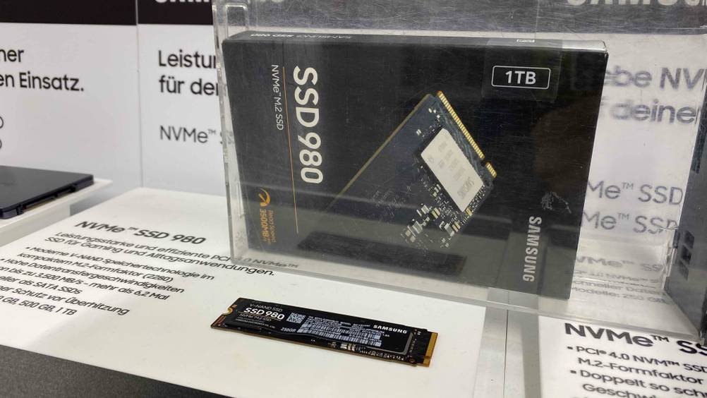 M.2-SSD getestet: Eine Festplatte in einer Infotafel eingebetet mit der Originalverpackung im Hintergrund.