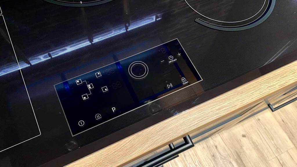 Detailansicht von oben auf das Kommandopaneel in eine Holzarbeitsplatte eines getesteten Kochfelds in 80 cm Größe der Marke Samsung.
