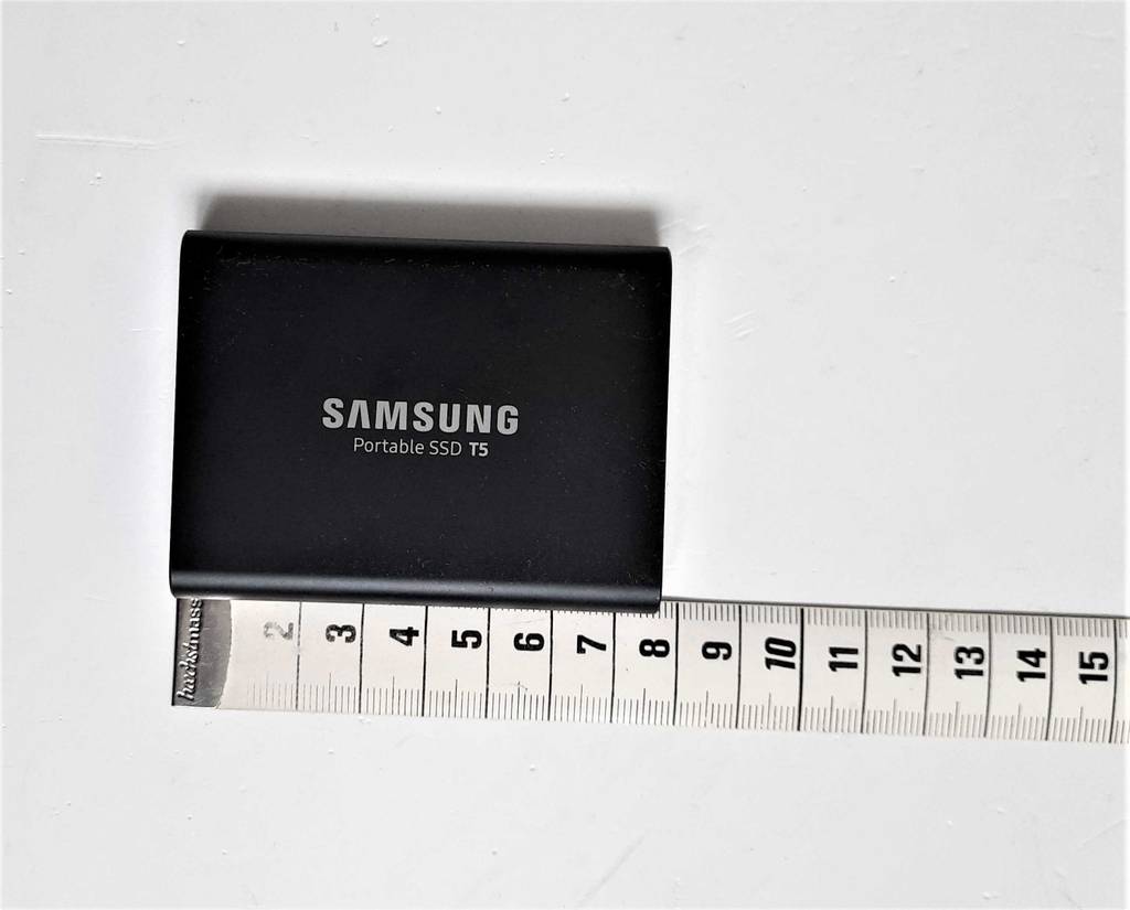 Eine schwarze externe SSD-Festplatte im Test liegt auf einer weißen Oberfläche und ist laut angelehntem Metermaß 8 cm lang.
