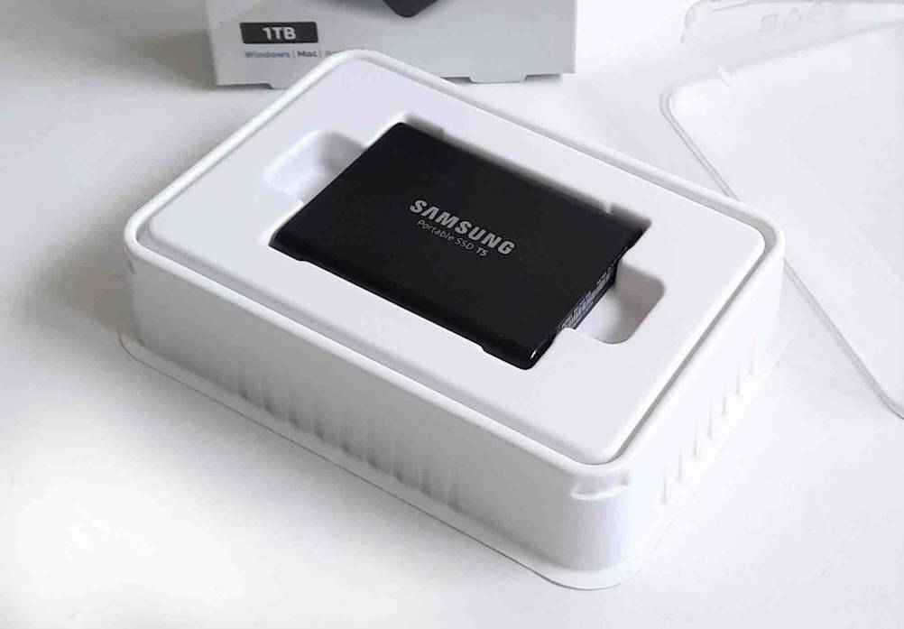Eine schwarze externe SSD-Festplatte im Test, der Marke Samsung, in einer weißen Originalverpackung liegt auf einer weißen Oberfläche.