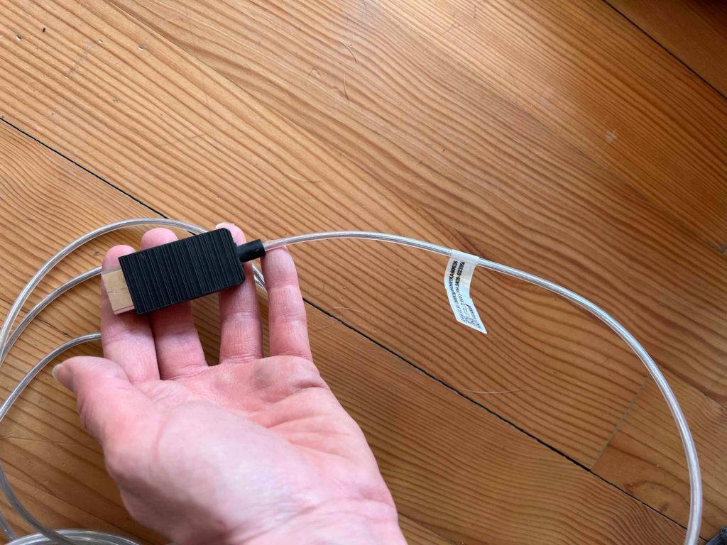 Eine Hand hält ein Anschlusskabel für einen getesteten 4K-Fernseher vor eine Holzfläche.